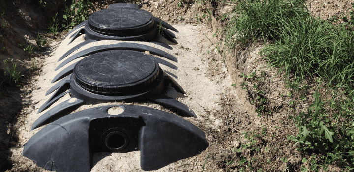 A septic tank sits in a hole, mostly covered by earth and sand in Ashford.