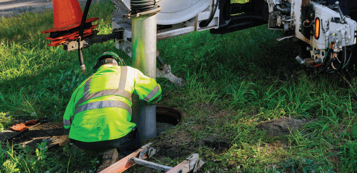A drainage engineer in hi-vis directs a large metal pump attached to a pump truck into a manhole in Gillingham.