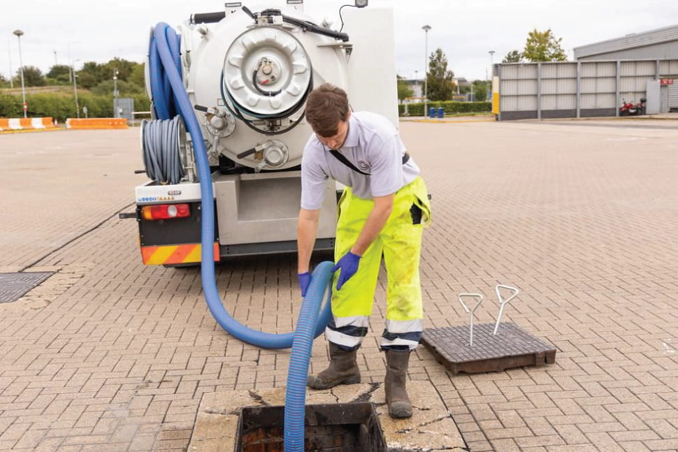 Chris uses a large suction hose to clear a manhole of dirty drain water in Newham.