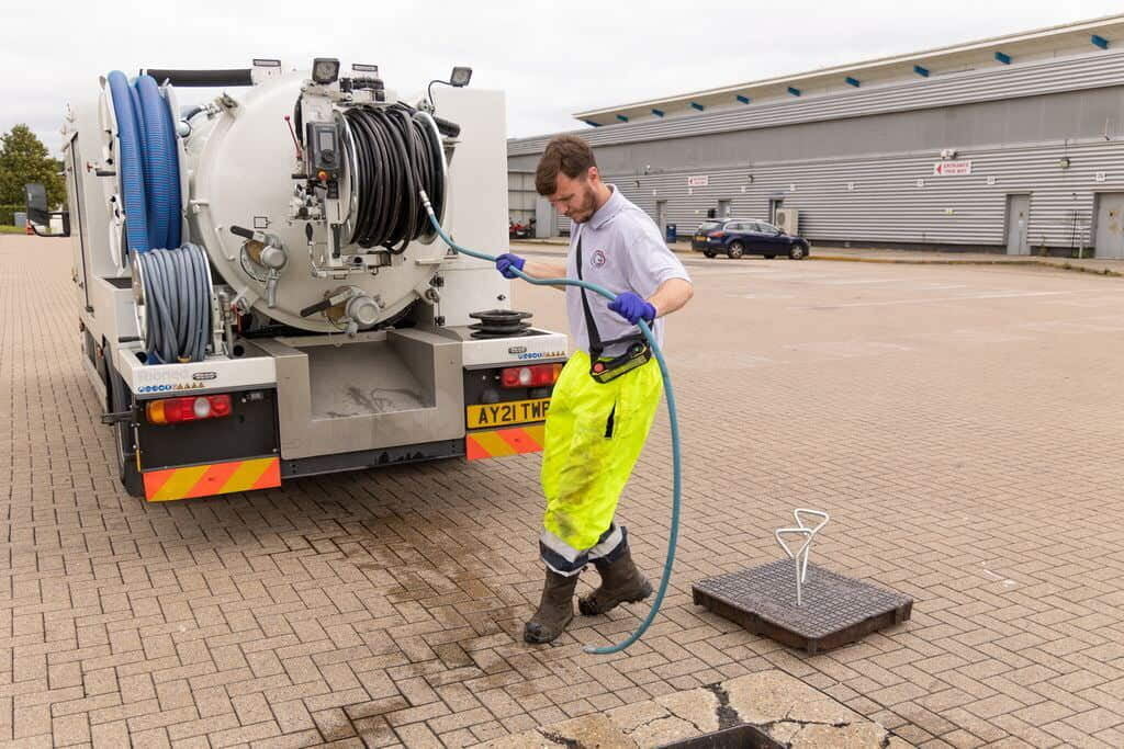 Grey-Water's Managing Director, Chris Guilfoyle using a long hose pipe on the back of a tanker truck to unblock a manhole.