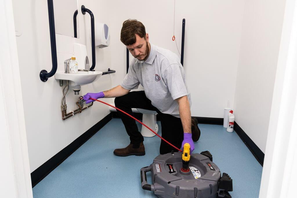 Chris from Grey-Water Drainage Solutions uses a tube to unclog a drain in a restroom in Maidstone.