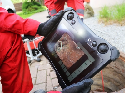 Gloved hands hold the CCTV screen, monitoring the inside of a drain.