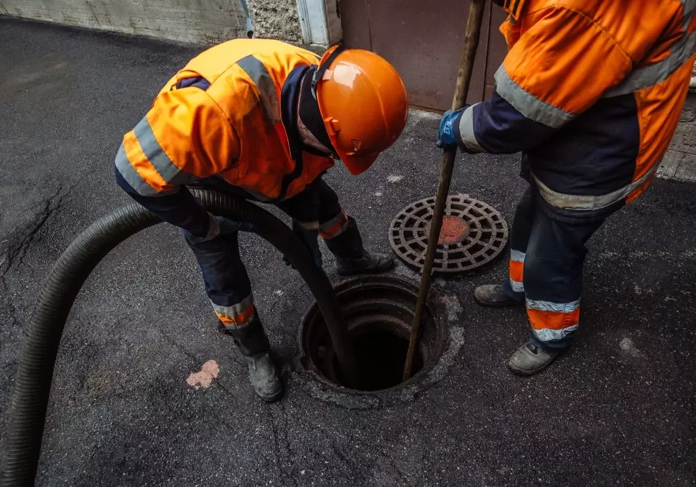 Sewer workers cleaning manhole and pumping.