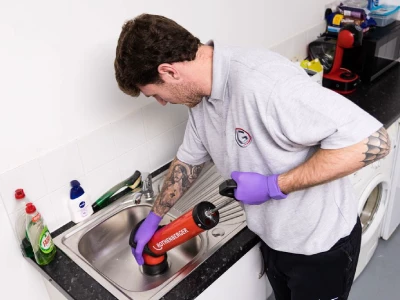 A member of the Grey-Water team uses a large plunging device to unblock a sink.