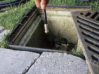 Drain rod being lowered into an open drain passage filled with debris.