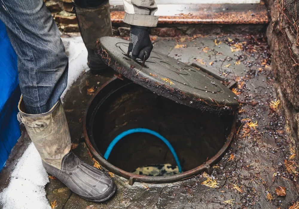 Drainage engineer in wellies and gloves lifting an inspection chamber cover to check a blocked outside drain