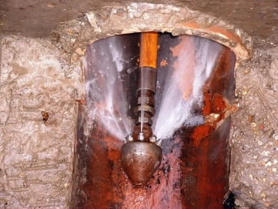 The inside of a drain shows a high-pressure jetting device shooting water from a nozzle to clear the drain.