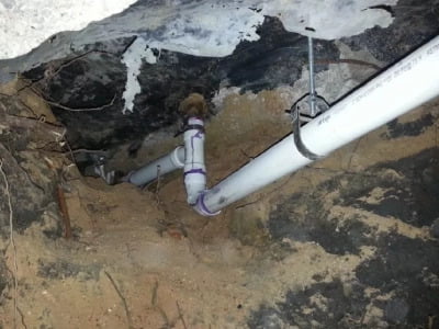 A pipe leads into the sandy ground. The rock and sediment surrounding it is off-colour, changing from a pale brown to black, with some white mould creeping in at the top.