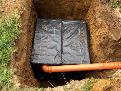 A covered soakaway placed in a trench with a drain pipe extending out of it.