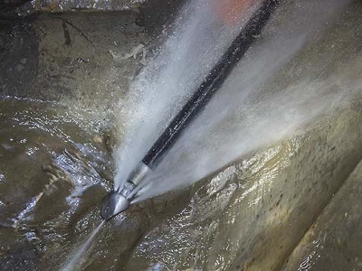 A jetting rod sprays water from in front and behind the nozzle to clear a drain.